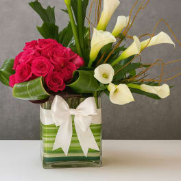 Pink roses and white calla lilies in a glass vase with a white bow
