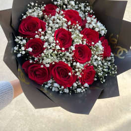 Handheld bouquet of red roses and white filler flowers wrapped in dark black paper
