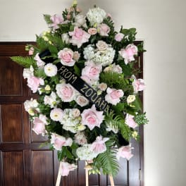 Large pink and white funeral wreath on an easel with a black ribbon