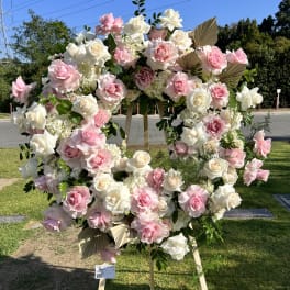 Large pink and white rose wreath on a wooden stand outdoors
