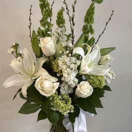 White lilies and roses arranged in a clear glass vase with a white ribbon