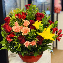 Red and peach roses with yellow lilies in a red vase