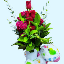 Bouquet of red roses in a white vase with a colorful teddy bear