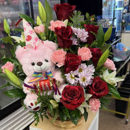 Basket arrangement with red roses, pink carnations, lilies, and a pink teddy bear
