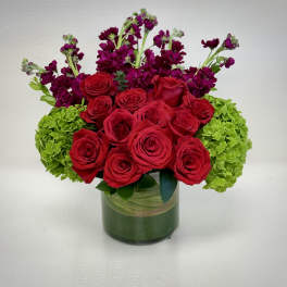 Red roses and purple flowers arranged in a glass vase with green hydrangeas