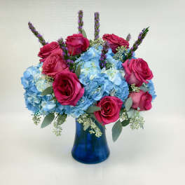 Arrangement of hot pink roses and blue hydrangeas in a dark blue glass vase