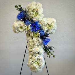 Standing cross-shaped spray of white flowers with bright blue blooms on a metal easel.
