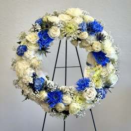 Standing wreath of white roses and mums with bright blue accents on a metal easel