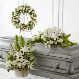 Sympathy set with white lilies and roses in a wreath, basket, and casket spray on a silver casket.