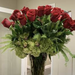 Tall vase arrangement of red roses, green orchids, and hydrangeas