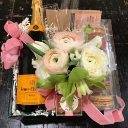Gift basket with flowers, champagne, macarons, and candy in a clear tray