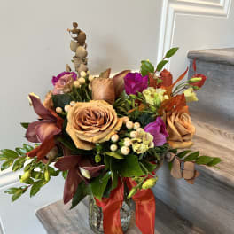 Mixed bouquet of peach roses and purple flowers in a glass vase with a red ribbon.