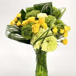 Tall arrangement of yellow roses and green blooms in a green glass vase