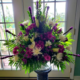 Large purple and white floral arrangement in a pedestal vase
