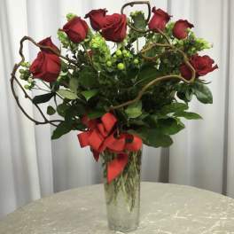 Red roses in a tall glass vase with a red ribbon