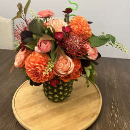 Orange and pink floral arrangement in a pineapple vase