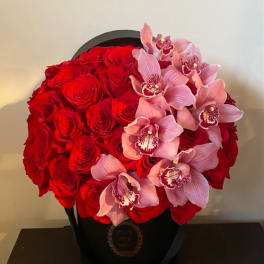 Red roses and pink orchids arranged in a black hatbox