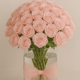 Bouquet of pale pink roses in a clear glass vase with a pink bow