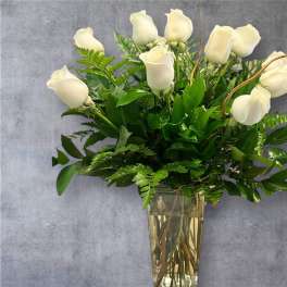 White roses in a clear glass vase with lush greenery
