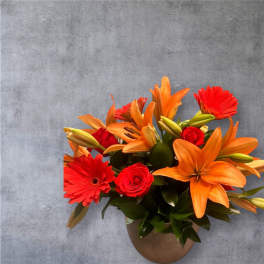 Orange lilies and red gerbera daisies in a brown vase