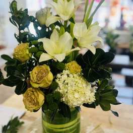 White lilies and yellow roses in a green glass vase