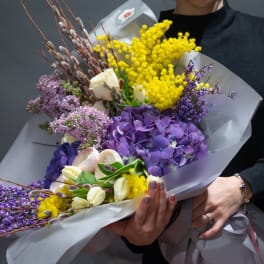 Bouquet of purple, yellow, and white flowers wrapped in pale paper