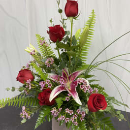 Tall arrangement of red roses and a pink stargazer lily in a square vase