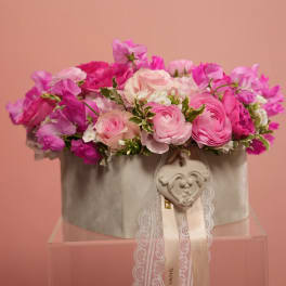 Pink floral arrangement in a gray hatbox with lace ribbon and heart ornament