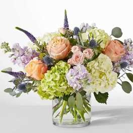Arrangement of peach roses, green and white hydrangeas, and lavender blooms in a clear glass vase