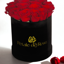 Round black hat box filled with tightly packed red roses with a gold logo on the front.