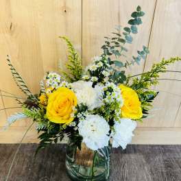 Yellow roses and white flowers in a glass vase with greenery