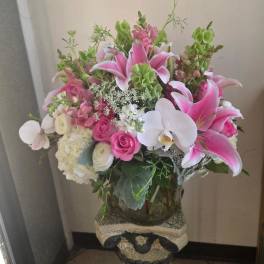 Tall arrangement of pink lilies, white orchids, roses, and hydrangeas in a clear glass vase