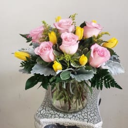 Pink roses and yellow tulips arranged in a clear glass vase