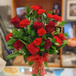 Red roses and carnations in a clear glass vase with a red ribbon