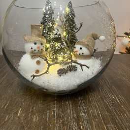 Two snowman figurines in a glass bowl with miniature trees and lights