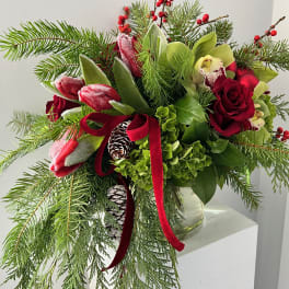 Holiday bouquet with red roses, tulips, and evergreen branches in a glass vase
