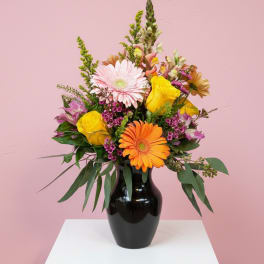 Mixed bouquet in a black vase with pink, yellow, and orange blooms