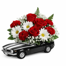 Red roses and white daisies arranged on a black toy car