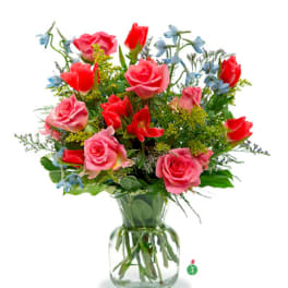 Mixed bouquet of pink roses, red tulips, and blue flowers in a clear glass vase