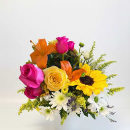 Mixed bouquet of roses, lilies, sunflowers, and daisies in a white vase