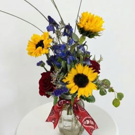Bouquet of sunflowers, blue flowers, and red roses in a glass jar vase