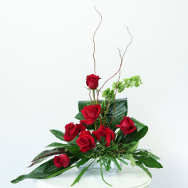 Red roses arranged in a clear glass vase with tall curly branches