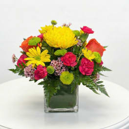 Colorful bouquet of yellow, pink, and orange flowers in a square glass vase