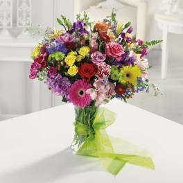 Colorful mixed bouquet with roses, gerbera daisies, and carnations in a clear vase with green ribbon
