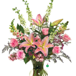 Tall arrangement of pink lilies and roses with white flowers in a clear glass vase