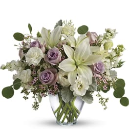 Lavender roses and white lilies arranged in a clear glass vase