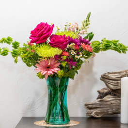 Colorful bouquet in a teal glass vase with candles beside it