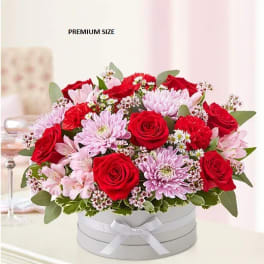 Red roses and pink chrysanthemums arranged in a white hat box with a ribbon