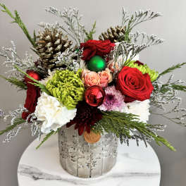 Holiday floral arrangement in a silver container with red roses and ornaments