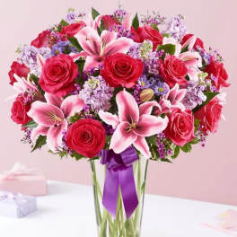 Bouquet of red roses and pink lilies in a clear glass vase with a purple ribbon